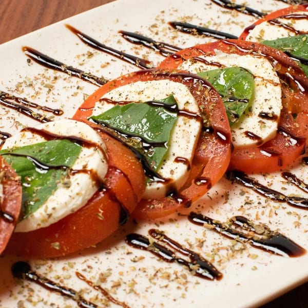 Caprese salad with sliced tomatoes, mozzarella, basil, balsamic glaze, and dried herbs on a white plate.