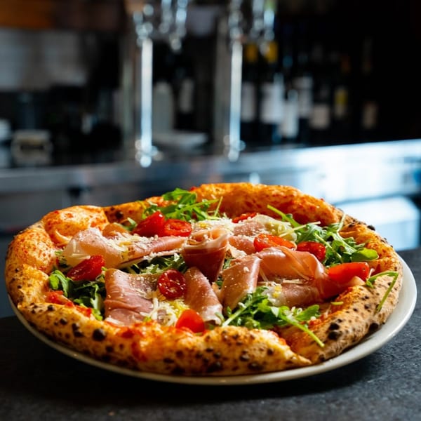 Neapolitan pizza with prosciutto, arugula, cherry tomatoes, and parmesan cheese on a white plate.