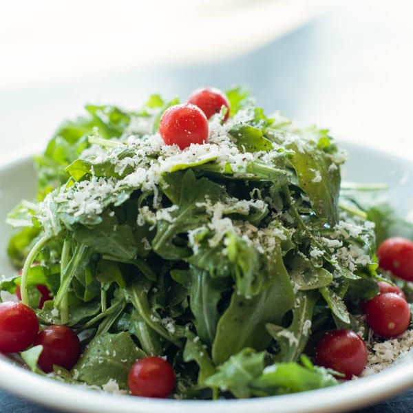 A fresh arugula salad with cherry tomatoes and grated cheese in a white bowl.