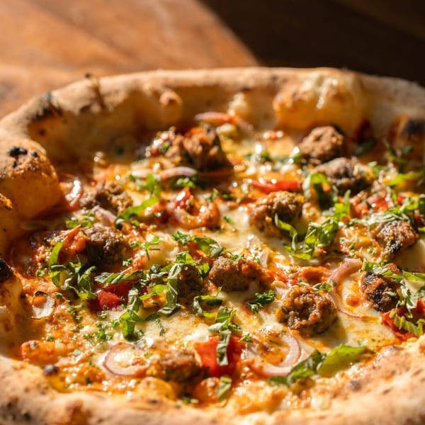 Close-up of a Piatto Neapolitan pizza with meatballs, red onions, and fresh basil.