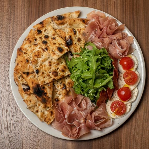 A Piatto Neapolitan Pizzeria antipasto platter with focaccia, prosciutto, arugula, and caprese salad.